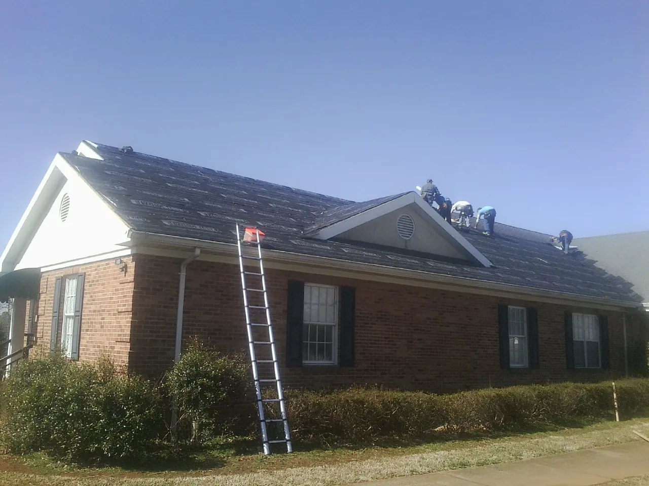 Crew tearing shingles off a brick ranch roof with a ladder set — Emergency Roof Repair work by our crew in Manton