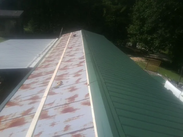 Old rusted panels beside newly installed green metal roofing — Wind Damage Roof Repair by Roofing Brothers in Manton