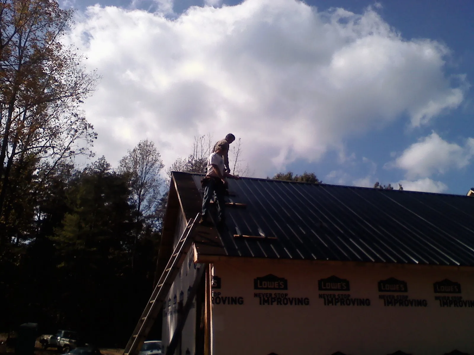 Roofer fastening dark metal panels high against a cloudy sky, from a Roof Inspection job in Manton