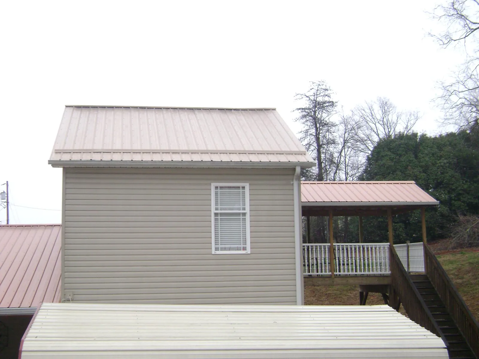 Tan metal roofs on a two story addition and attached porch, from a Roof Replacement job in Manton